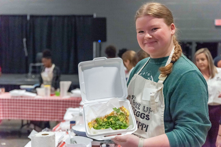 A girl holds a white tray of food and smiles. 