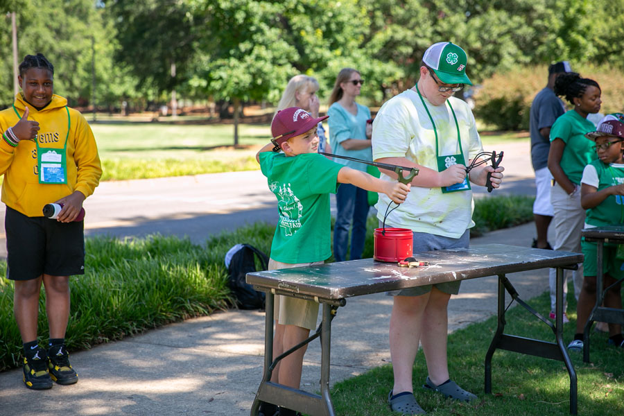 One boy, on the far left, gives a thumbs up, while another, in the middle, aims a slingshot.