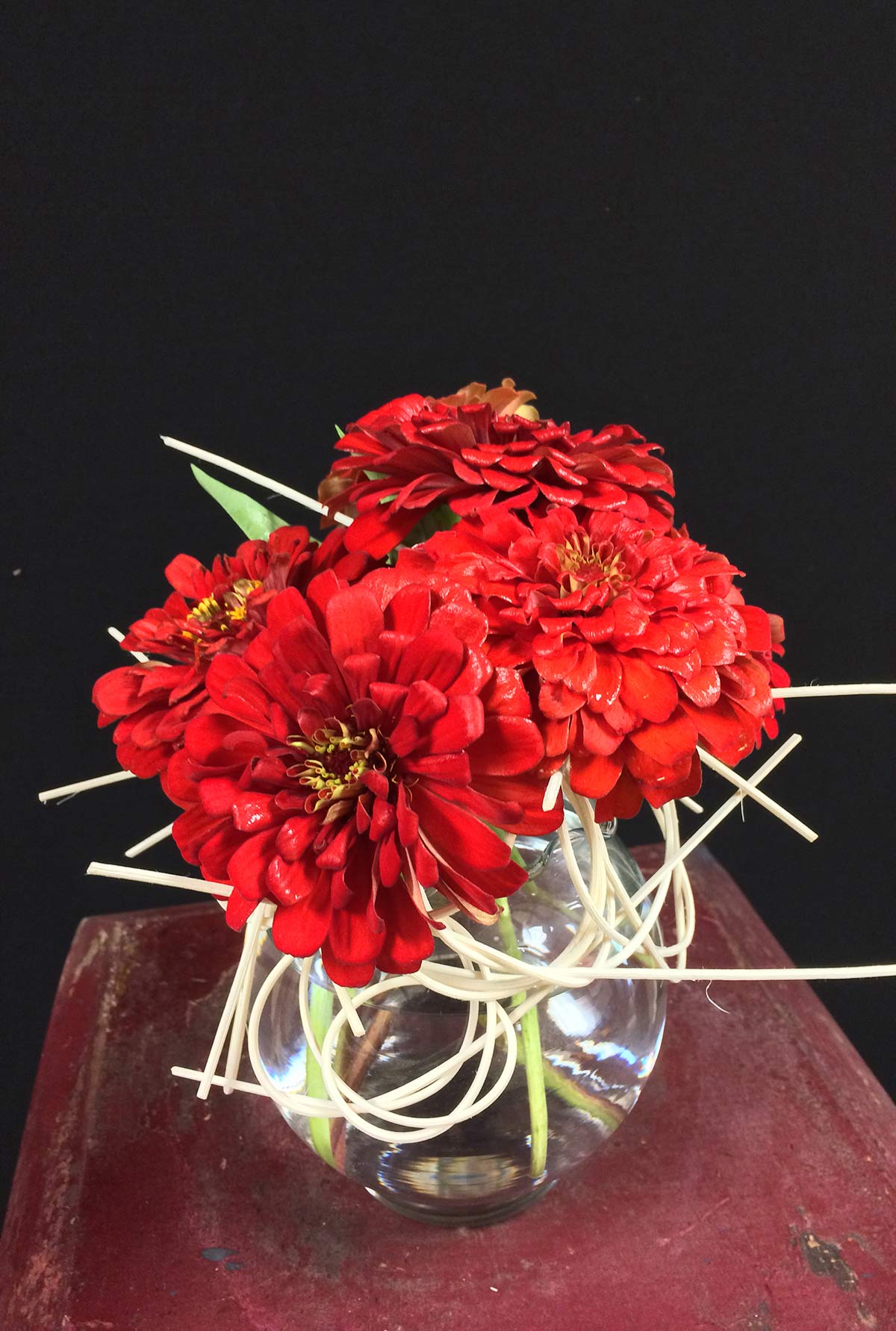 Red zinnias placed into the floral frog. The wicker frog is visible and part of the overall design.