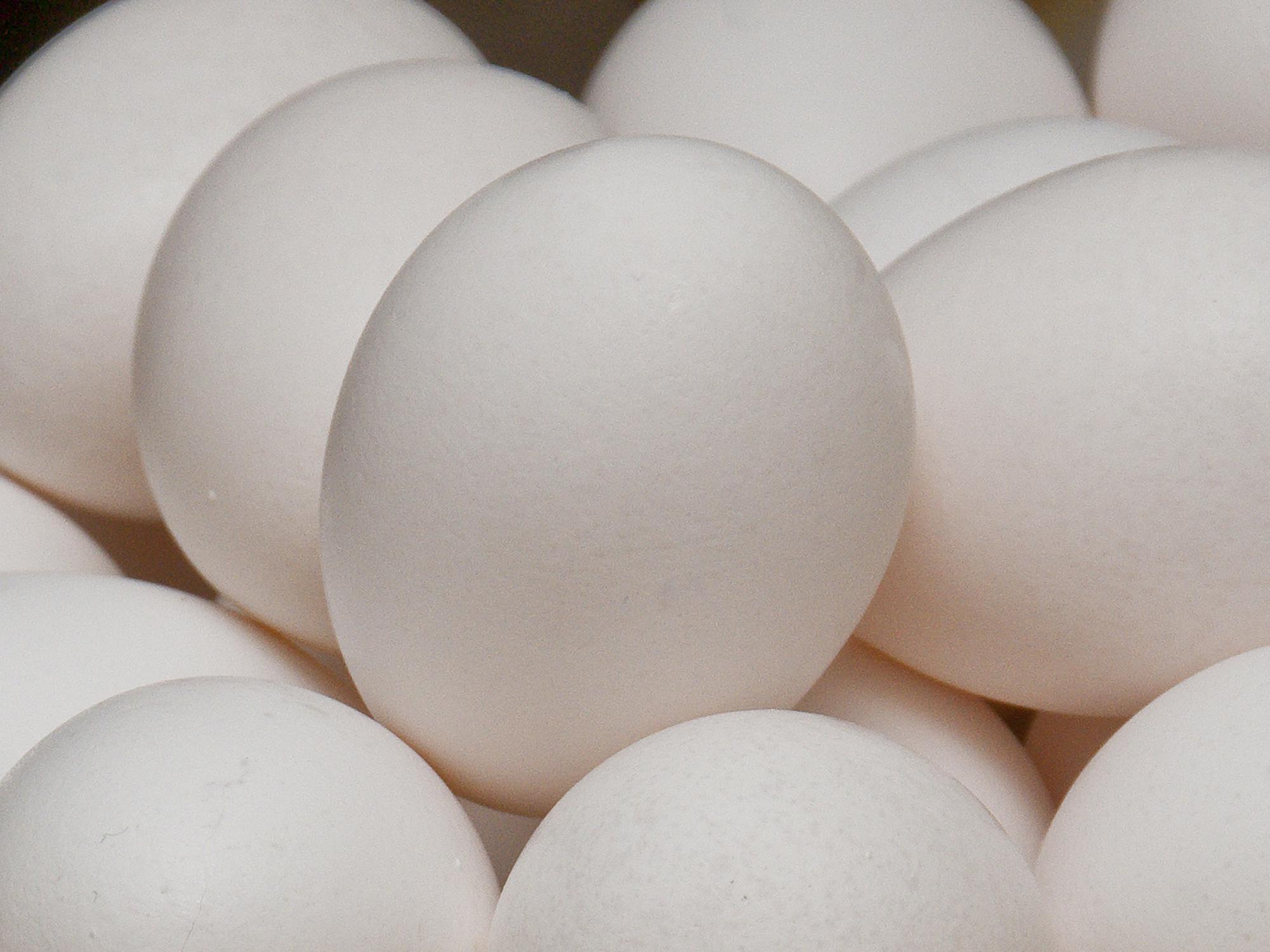 A close up of white eggs stacked in a bowl with other white eggs.