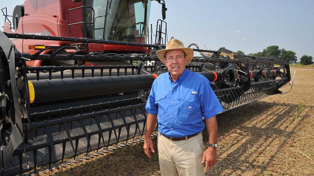 A man standing in a field next to farming equipmen.