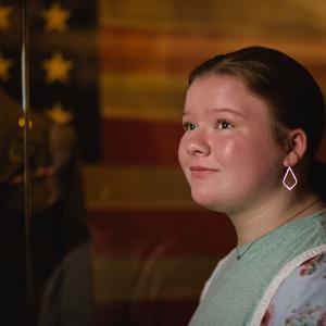 A girl smiling in front of an American flag.