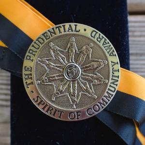 A silver medallion, engraved with people holding hands and looped with a gold and black ribbon, lying on a black box.