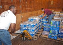 Two men move cases of bottled water in a storehouse.