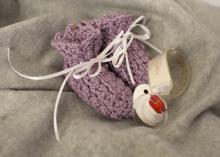 Still life arrangement of a pair of knitted infants booties, a hospital ID band and a pacifier.