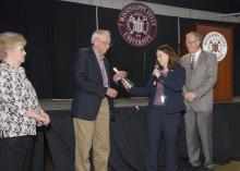 Woman handing man silver cowbell and shaking his hand.