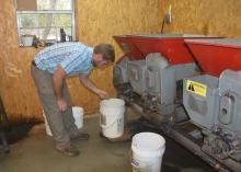 Man leans over a 5-gallon bucket placed under a large mechanical unit inside a building.