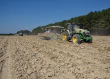 Two tractors pull harvest carts across a dusty field.