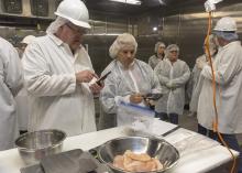 Two people in protective gear work with meat on a table.