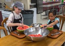 Two children make melon balls from a watermelon.