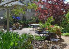 Tables and chairs are on a patio in a backyard garden.