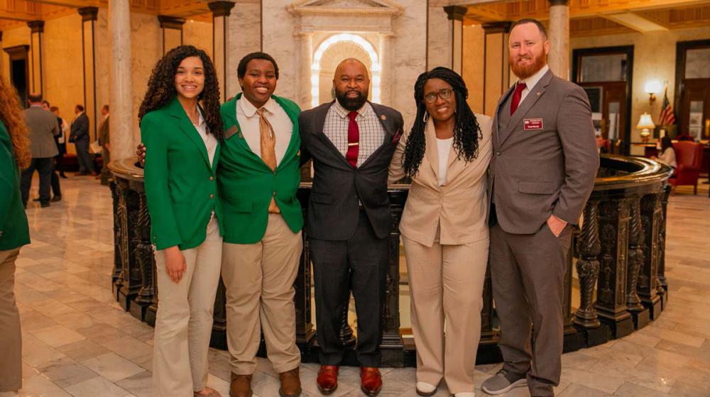 Five people, including two teens in green 4-H blazers, smile for a group photo.