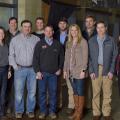 Ten adults, including 3 women and 7 men, stand smiling in front of a Mississippi Farmers’ Market banner.