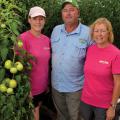 A young woman with an older man and woman standing next to a tomato plant.