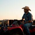 A man wearing a cowboy hat sits on an ATV in front of cows.