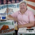 Woman pictured with arms resting on boxes labeled “Mississippi Sweet Potatoes.”