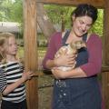 A woman holds a brown and white chicken while a young girl looks on.