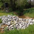 A pile of large gray rocks stretches across a ditch in a country setting.