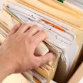 A man’s hand reaches into a box of files, pulling back the corner of one folder.