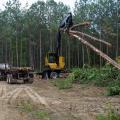 A large, yellow machine lifts downed trees to load onto a log truck.