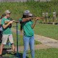 Teenagers at a shooting sports competition aim shotguns at targets.