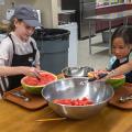 Two children make melon balls from a watermelon.