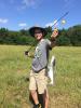 A teenage boy proudly holds up a catfish on his fishing line.