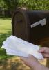 A pair of hands holds a stack of mail taken from a mailbox.