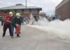 Two men wearing hard hats and masks activate a fire extinguisher as MyPI training participants watch. 