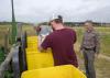 Two young men pour seed into bright yellow bins while a man watches.