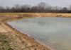 A partially filled pond with minimal plant life visible around the banks.