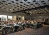 Hundreds of people in rows form an audience for a speaker in a large, open room.