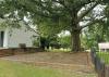 A large tree looms over a white house and a brick patio area.