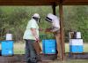 Two men in beekeeping attire examine bee hive boxes.