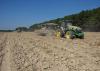 Two tractors pull harvest carts across a dusty field.