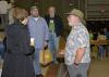 A man in a gardening hat stands and talks to three adults, with several others milling about in the background.