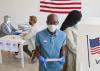 Voter wearing mask, standing by booth and looking at camera.