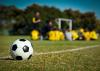 A soccer ball sits in the foreground with a soccer team and coach in the background.